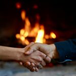 Close-up of a handshake in front of a warm, glowing fireplace, symbolizing agreement and warmth.