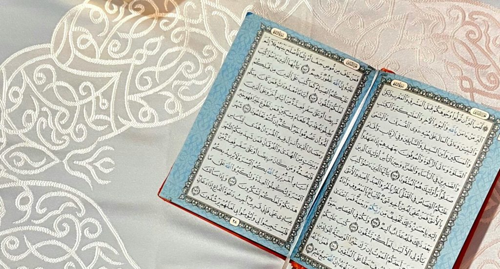 Quran open on a beautifully patterned cloth, illuminated by a traditional lantern.
